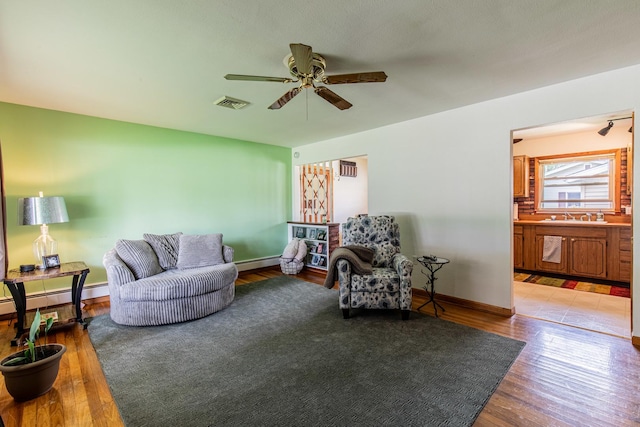 living area with baseboard heating, a ceiling fan, wood finished floors, and visible vents