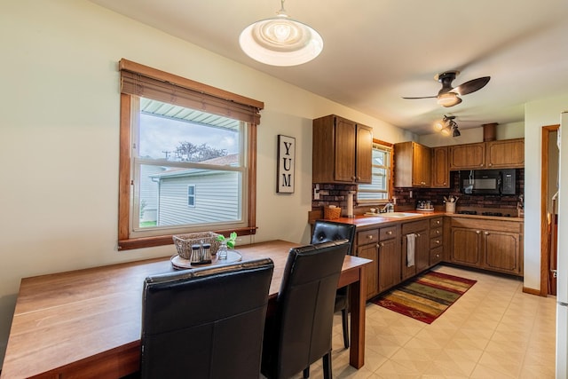 kitchen featuring a ceiling fan, backsplash, brown cabinets, a sink, and black appliances