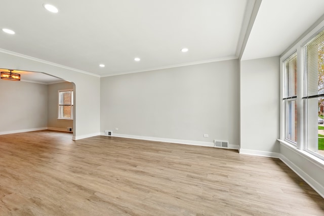 empty room with light wood-style floors, arched walkways, baseboards, visible vents, and ornamental molding