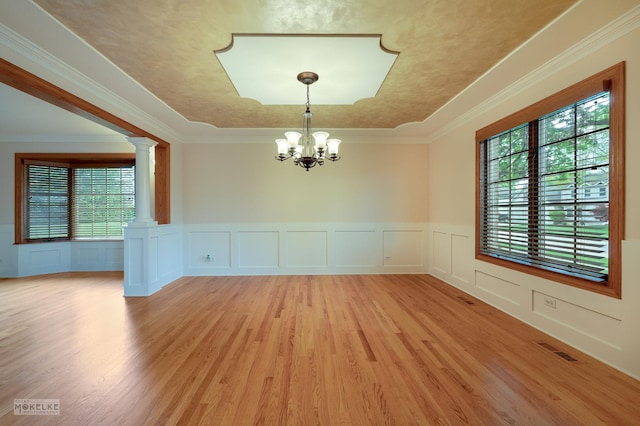 empty room with wainscoting, a decorative wall, ornate columns, a chandelier, and light wood-style flooring