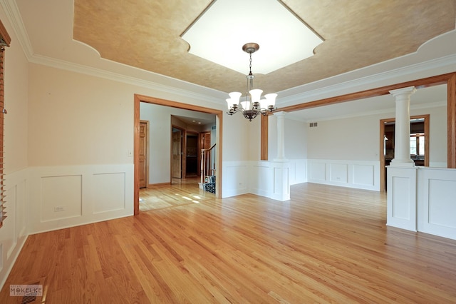 empty room with decorative columns, a raised ceiling, light wood finished floors, a chandelier, and a decorative wall
