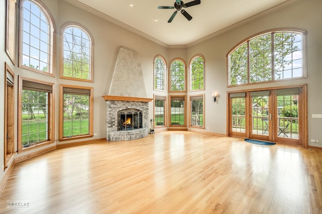 unfurnished living room featuring a fireplace, a high ceiling, ceiling fan, and wood finished floors
