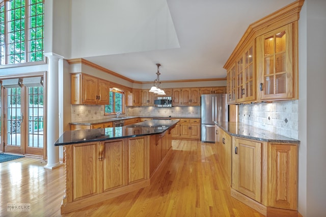 kitchen featuring glass insert cabinets, a center island, light wood finished floors, appliances with stainless steel finishes, and backsplash