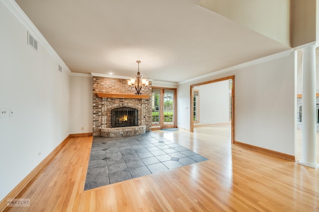 unfurnished living room featuring visible vents, a brick fireplace, wood finished floors, a notable chandelier, and ornate columns