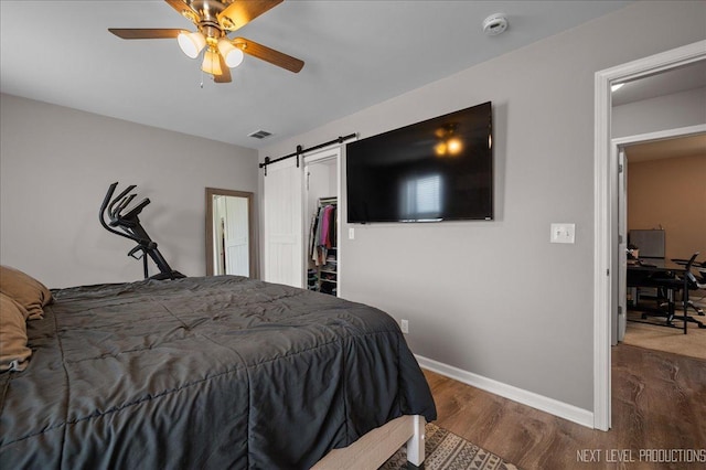 bedroom featuring wood finished floors, a barn door, baseboards, a ceiling fan, and a walk in closet