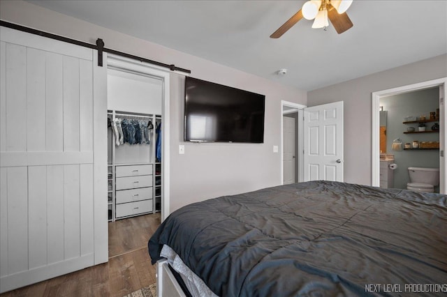 bedroom with wood finished floors, a barn door, a closet, ceiling fan, and ensuite bath