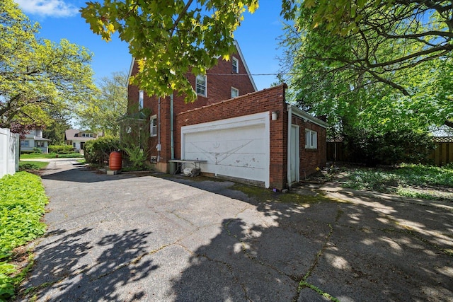 view of property exterior featuring brick siding, a garage, fence, and driveway