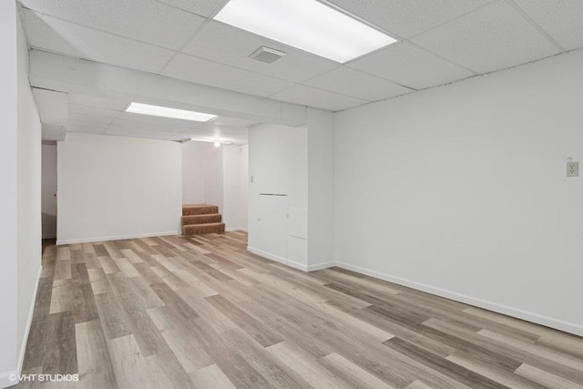 finished below grade area featuring stairway, a paneled ceiling, light wood finished floors, and baseboards