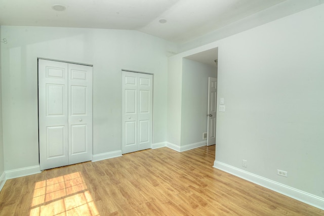 2205 Gladstone Ct, Glendale Heights, IL 60139 - unfurnished bedroom featuring multiple closets, vaulted ceiling, light wood-type flooring, and baseboards