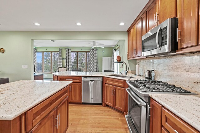 kitchen featuring appliances with stainless steel finishes, a sink, recessed lighting, brown cabinets, and light stone countertops