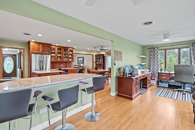 kitchen featuring ceiling fan, stainless steel refrigerator, a desk, a kitchen island, and light wood-style flooring