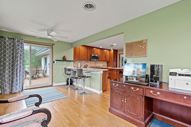 kitchen with stainless steel microwave, a ceiling fan, an office area, decorative backsplash, and a kitchen breakfast bar