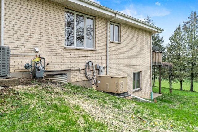 view of side of property with central AC unit, brick siding, and a yard