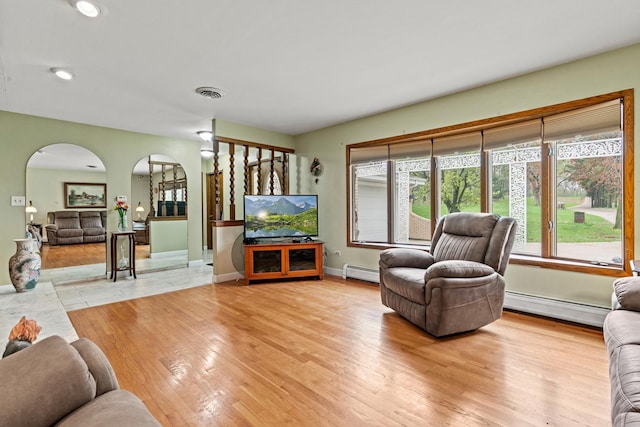 living room with arched walkways, a baseboard radiator, baseboards, light wood-type flooring, and recessed lighting