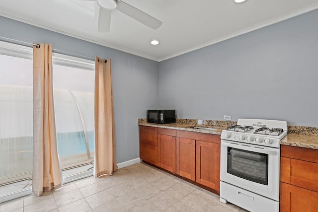 kitchen featuring gas range gas stove, black microwave, brown cabinetry, ceiling fan, and crown molding