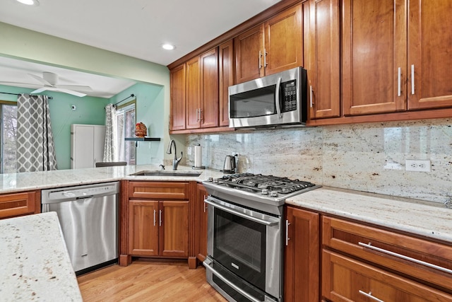 kitchen with stainless steel appliances, a sink, brown cabinetry, light wood-style flooring, and tasteful backsplash