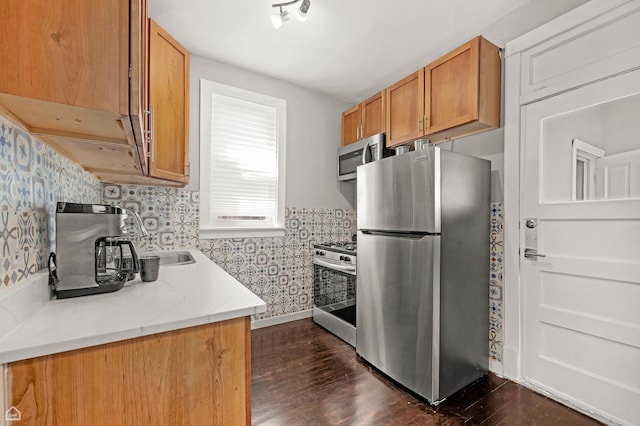kitchen featuring appliances with stainless steel finishes, wallpapered walls, dark wood-type flooring, light countertops, and brown cabinets
