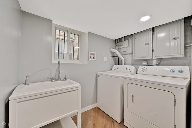 washroom with electric panel, washer and dryer, light wood finished floors, and baseboards