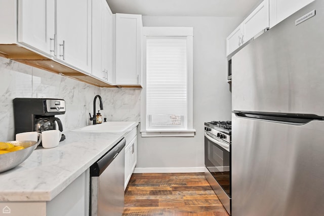 kitchen with appliances with stainless steel finishes, dark wood-type flooring, decorative backsplash, a sink, and white cabinets