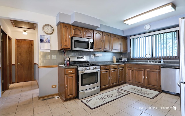 kitchen with stainless steel appliances, a sink, dark countertops, tasteful backsplash, and light tile patterned floors