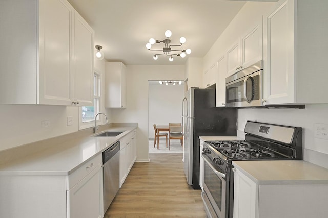 kitchen with white cabinets, an inviting chandelier, a sink, stainless steel appliances, and light wood-type flooring