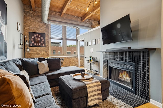 living area with a towering ceiling, a fireplace, beamed ceiling, brick wall, and wood ceiling