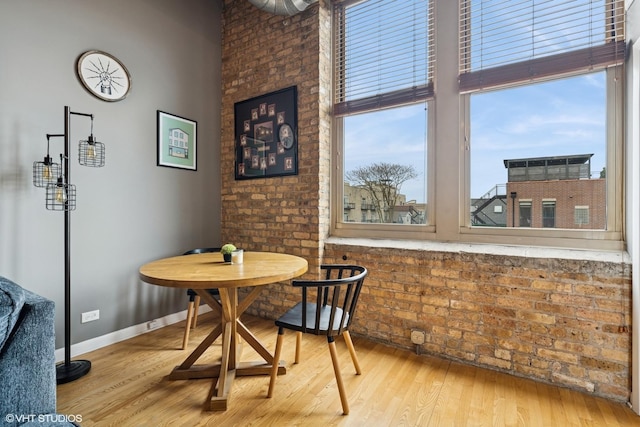dining room featuring baseboards, brick wall, a high ceiling, and wood finished floors