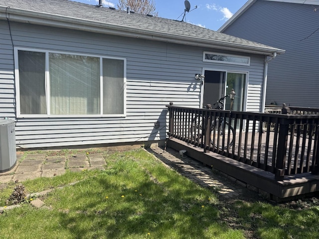 rear view of house featuring a yard, cooling unit, a wooden deck, and roof with shingles
