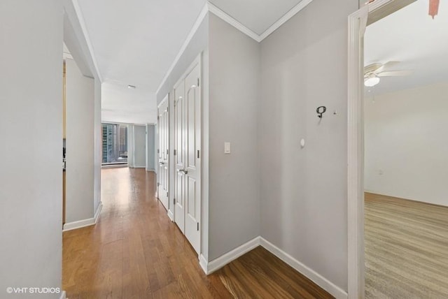 corridor featuring wood finished floors, ornamental molding, and baseboards