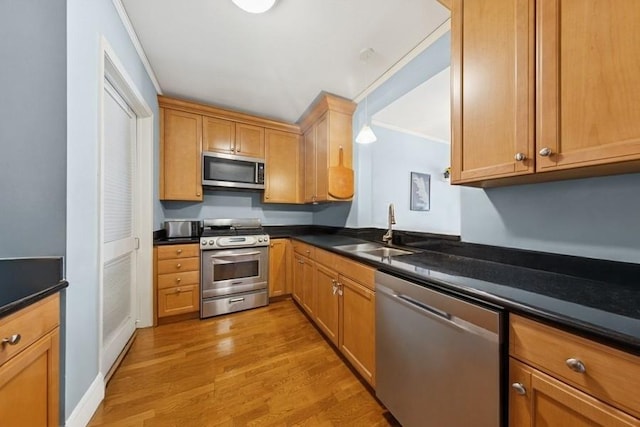 kitchen featuring stainless steel appliances, a sink, wood finished floors, and dark countertops