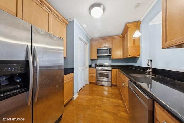 kitchen with stainless steel appliances, a sink, light wood-style floors, and decorative light fixtures