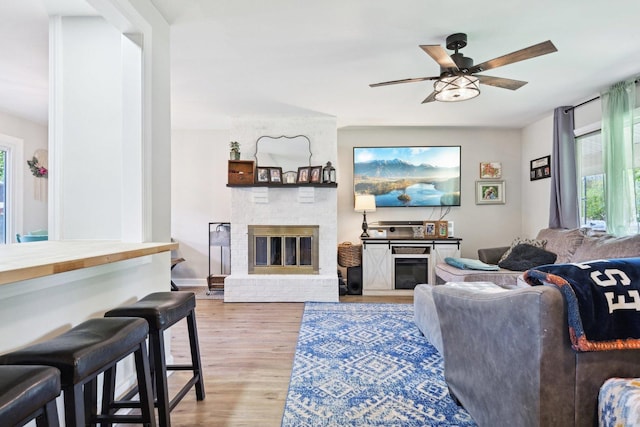 living room with a fireplace, light wood-style flooring, and a ceiling fan