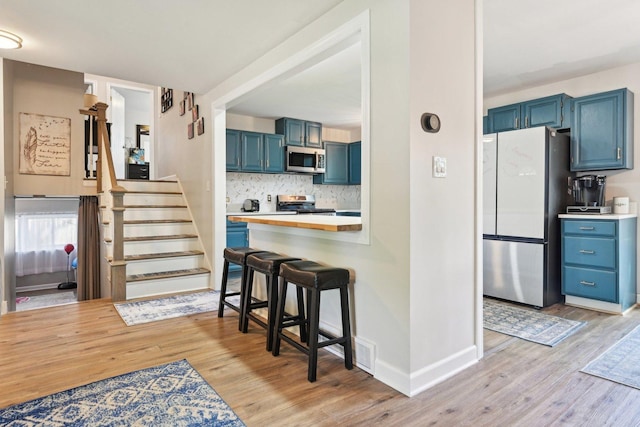 kitchen with appliances with stainless steel finishes, blue cabinetry, and light wood finished floors