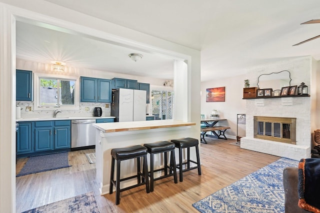 kitchen with freestanding refrigerator, blue cabinets, stainless steel dishwasher, a kitchen bar, and light countertops