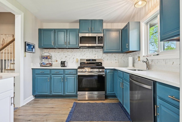 kitchen featuring stainless steel appliances, light wood-style flooring, a sink, light countertops, and backsplash