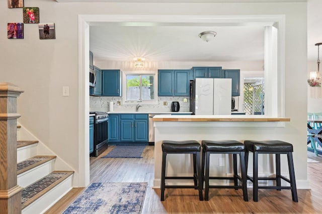 kitchen with stainless steel appliances, blue cabinetry, a kitchen bar, light wood finished floors, and decorative backsplash
