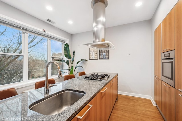 kitchen with brown cabinets, appliances with stainless steel finishes, a sink, island range hood, and visible vents