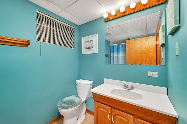 bathroom with vanity, toilet, a shower with shower curtain, baseboards, and a drop ceiling