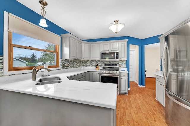 kitchen featuring decorative backsplash, light countertops, a sink, appliances with stainless steel finishes, and gray cabinetry