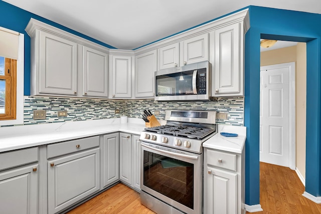 kitchen featuring light countertops, gray cabinets, tasteful backsplash, light wood finished floors, and stainless steel appliances