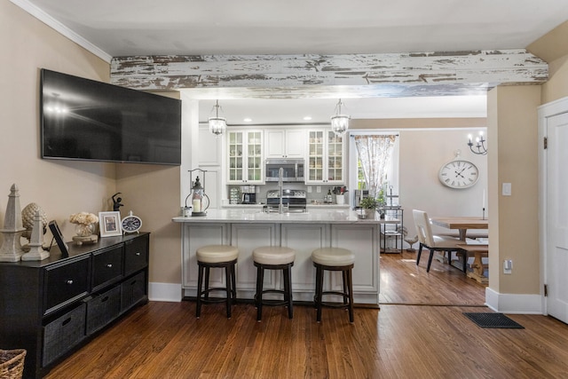 kitchen with a peninsula, stainless steel appliances, dark wood-style floors, a breakfast bar, and a chandelier