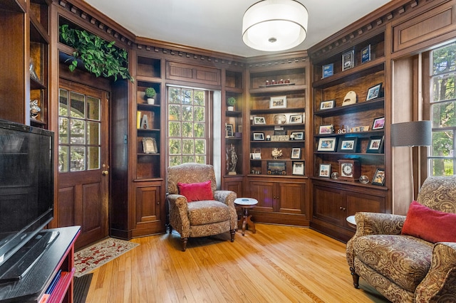 sitting room featuring light wood-style floors, ornamental molding, and built in shelves