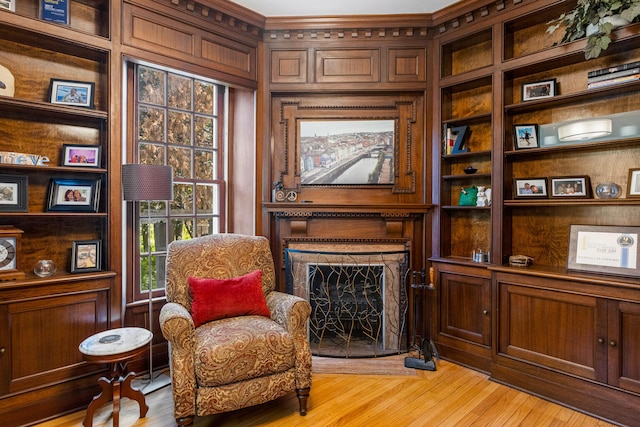 sitting room featuring built in shelves, light wood-type flooring, a fireplace with flush hearth, and wooden walls