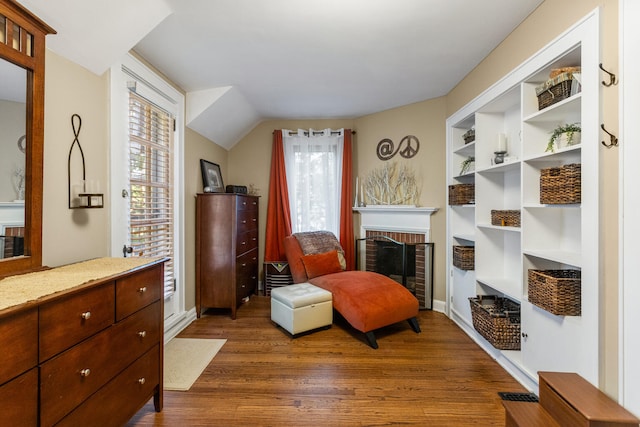 sitting room with dark wood-type flooring, a fireplace, built in shelves, and lofted ceiling