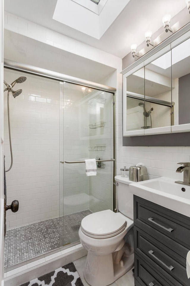 bathroom with a skylight, a shower stall, toilet, and vanity