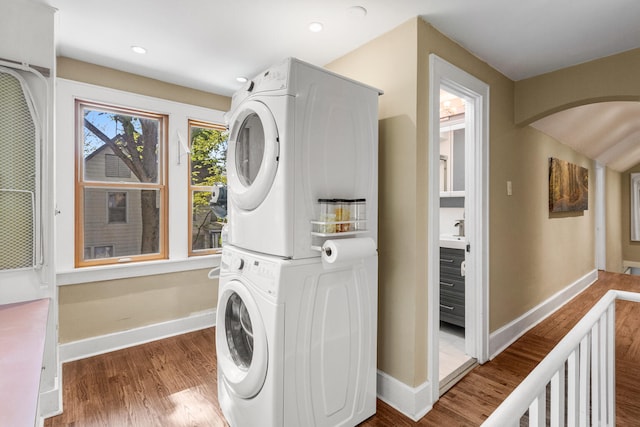 washroom featuring stacked washer and clothes dryer, baseboards, arched walkways, wood finished floors, and recessed lighting