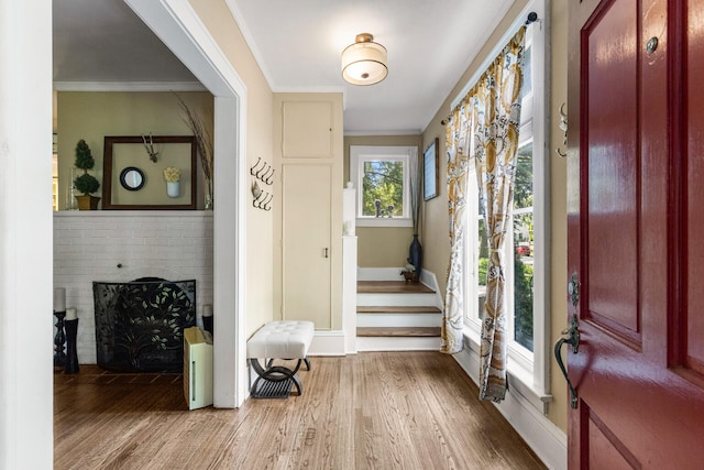 entrance foyer with wood finished floors, a fireplace, stairs, ornamental molding, and baseboards
