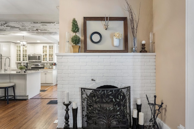detailed view of stainless steel appliances, a brick fireplace, wood finished floors, and a sink