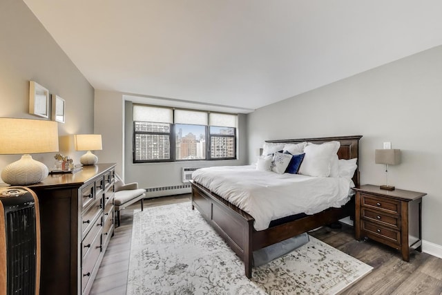 bedroom featuring wood finished floors, baseboards, multiple windows, and a baseboard heating unit