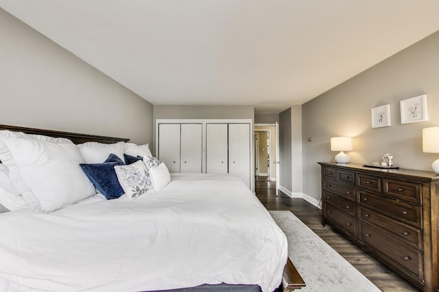 bedroom with two closets, baseboards, and dark wood-type flooring